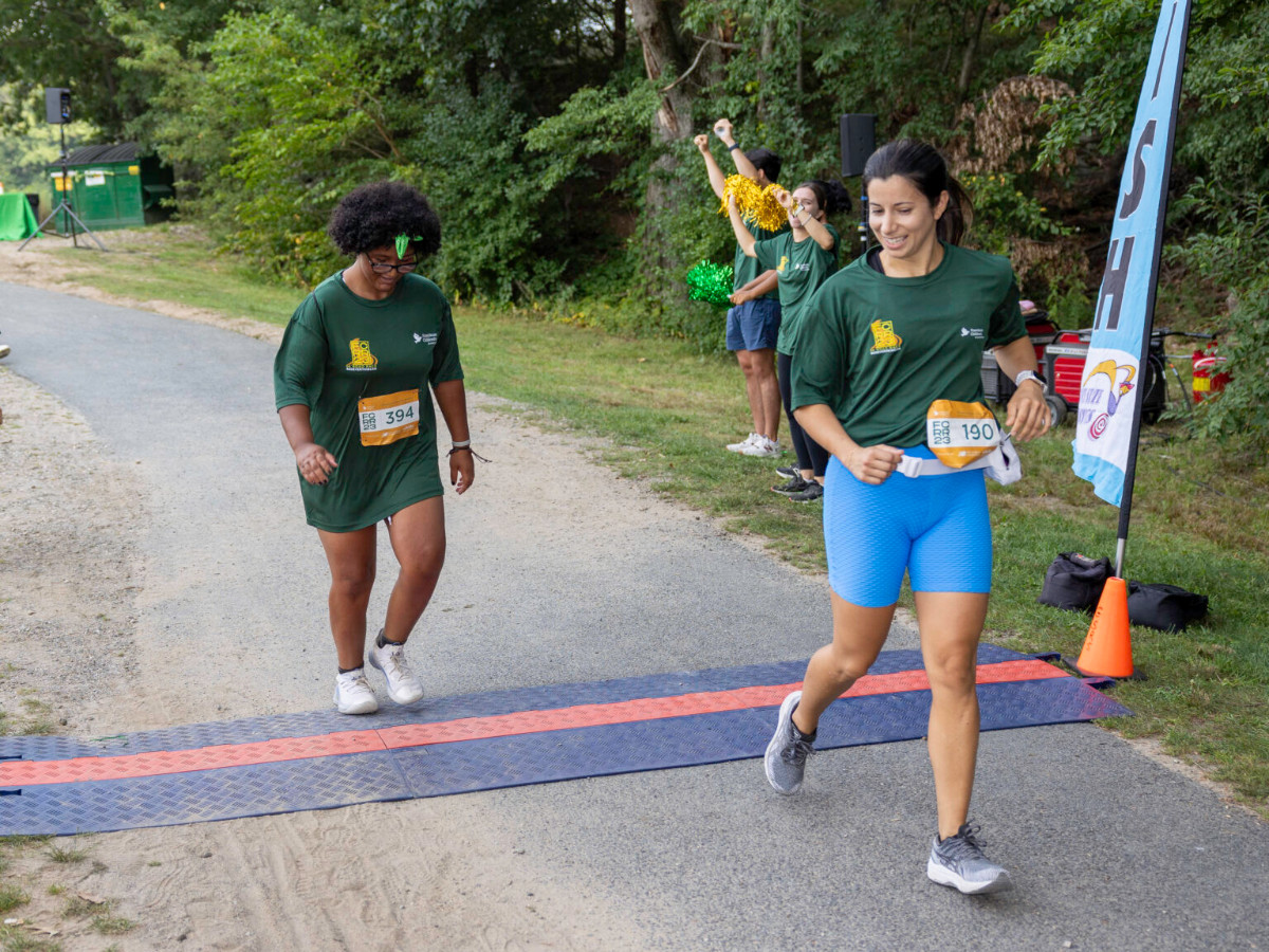 a girl crossing the finish line of a race while a woman cheers her on from slightly ahead of her