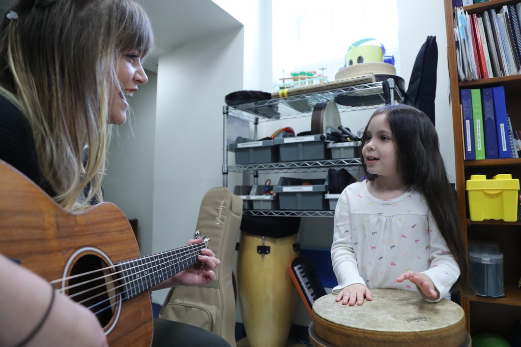 a girl playing the drums with her teacher playing the guitar