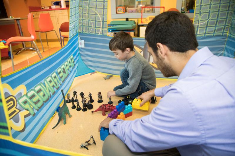 a boy playing with figurines while an adult watches