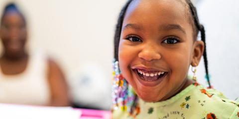 A young girl in a hospital johnnie smiles wide as she looks at the camera